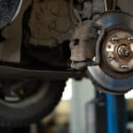 car mechanic worker repairing suspension of lifted automobile at auto repair garage shop station