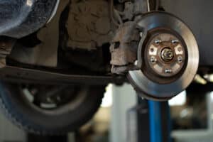 car mechanic worker repairing suspension of lifted automobile at auto repair garage shop station